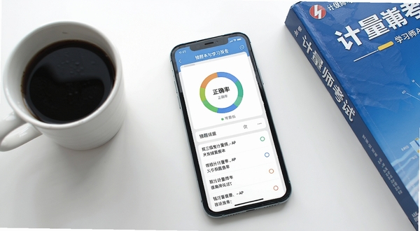 一二级计量师APP错题本与学习报告界面,手机屏幕显示环形正确率图表和错题列表,背景为简洁的白色办公桌面,旁边放着一杯咖啡和计量师考试教材,画面明亮清晰