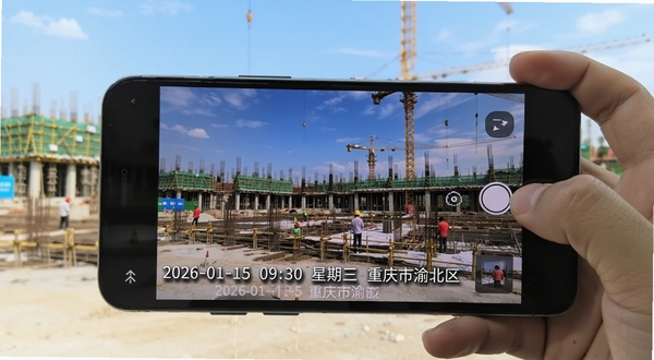 开心水印相机实时水印叠加功能展示,画面中一部安卓手机正在拍摄建筑工地场景,照片底部清晰显示“2026-01-15 09:30 星期三 重庆市渝北区”等水印信息,水印字体为白色带阴影,背景为蓝天下的施工现场,整体构图体现真实记录感