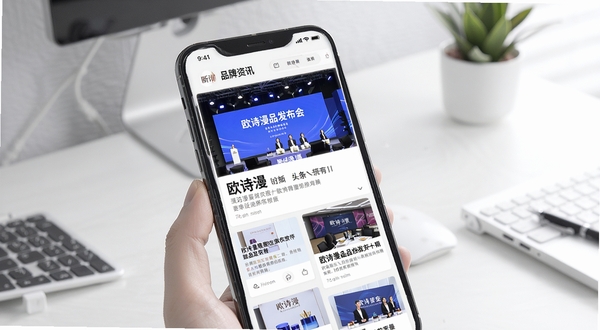 欧诗漫头条品牌资讯页面展示,画面主体为手机界面呈现新闻卡片式布局,背景为简洁的办公桌面环境,屏幕中显示欧诗漫新品发布会现场图片与标题文字,风格商务清新