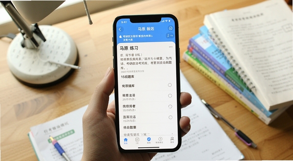考研政治刷题库app主界面展示,手机屏幕显示马原章节练习题目与选项,背景是书桌与考研资料,画面明亮清晰,突出学习氛围
