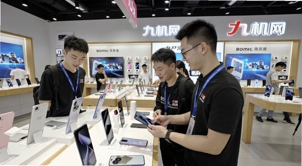 九机网线下门店服务场景,画面展示明亮的手机卖场内部,店员正在为顾客介绍手机,背景有九机网品牌标识,适配Boogu模型生成
