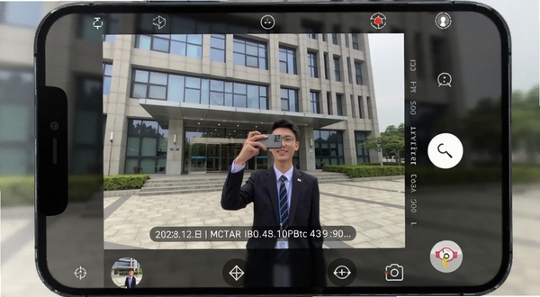 打卡定位水印相机拍摄界面,手机屏幕显示相机取景框,画面中一栋办公楼前有员工正在拍照,照片底部叠加时间地点水印信息,界面按钮布局清晰,突出水印模板选择功能