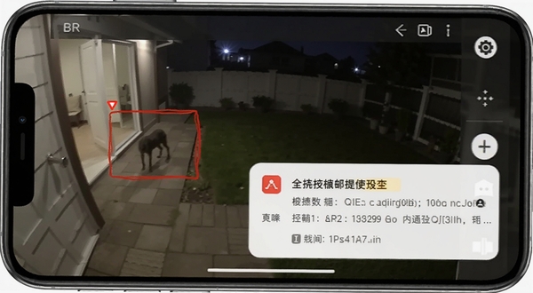 手机屏幕显示监控画面中有移动物体被红色方框标记,旁边弹出报警通知,背景是夜晚的庭院,手机监控软件界面,突出移动侦测报警功能