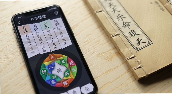 诠天八字排盘界面特写,手机屏幕显示四柱八字表格与五行圆环图,天干地支清晰排列,背景为浅色木质桌面,旁边放置一本打开的线装古籍,光线柔和,画面呈现专业且宁静的命理学习场景