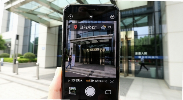 速改水印相机拍照界面展示实时定位与天气信息,画面主体为手机取景框内显示当前街道名称和温度图标,背景为写字楼入口区域,光线充足,突出外勤打卡场景的真实感
