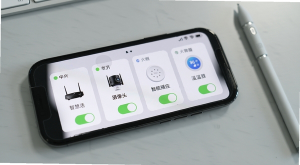 中兴智慧生活APP设备管理界面特写,手机屏幕显示四个设备卡片横向排列,分别标注路由器、摄像头、智能插座、温湿度传感器,每个卡片带有状态指示灯与快捷开关,背景为浅灰色办公桌面,画面右侧放置一支触控笔,整体构图干净利落