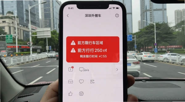深圳外地车限行提醒功能界面,手机屏幕上显示红色预警提示框,标注前方限行区域与剩余限行时间,背景为深圳市区道路实景,画面风格写实清晰,突出警示效果