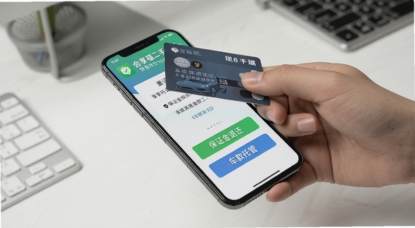 一只手拿着银行卡靠近手机,手机屏幕显示会享福二手车App的资金托管页面,有“保证金退还”“车款托管”等中文按钮,背景是简洁的办公桌面,画面风格干净商务