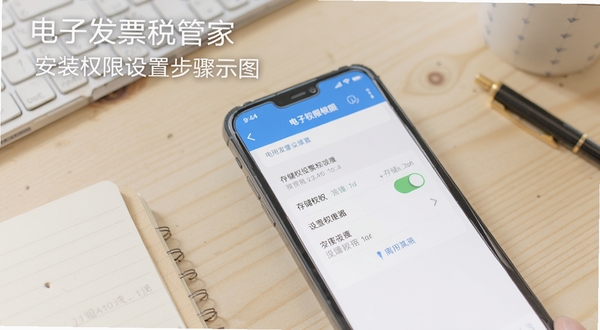 电子发票税管家安装权限设置步骤示意图,手机屏幕显示应用权限管理页面,存储权限开关处于开启状态,背景为浅色木质桌面与文具,画面简洁清晰,适合教程配图