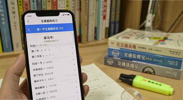 安驾课堂全真题库练习界面,手机屏幕显示科目一题目与解析内容,旁边有章节分类列表,背景为书房学习环境,画面中有交通法规书籍与荧光笔,光线明亮柔和