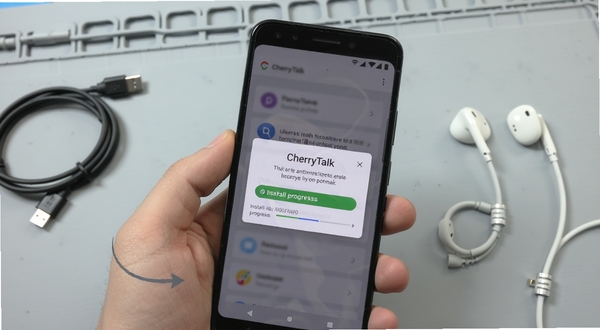 CherryTalk安装与权限设置操作场景图,画面中央为手持安卓手机的特写,屏幕显示权限授权弹窗与安装进度条,背景为简洁的浅灰工作台,旁边放置数据线与耳机等配件,整体风格写实清晰,突出操作指引感
