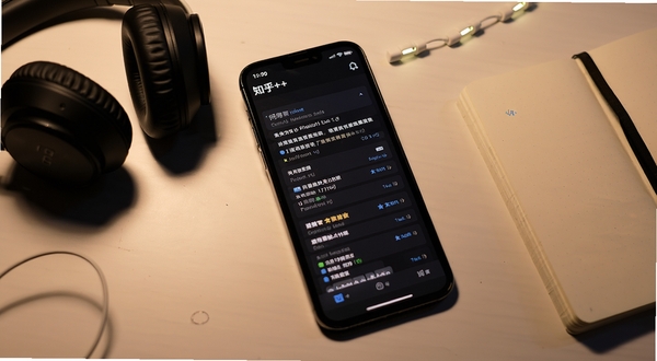 知乎++夜间阅读模式界面,深色背景中显示问答正文,手机置于桌面,旁边有耳机与笔记本,氛围安静舒适