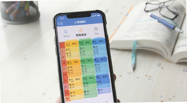 上课软件界面中色彩分明的周课程表展示,手机屏幕特写,背景为书桌与课本,光线柔和,画面干净整洁
