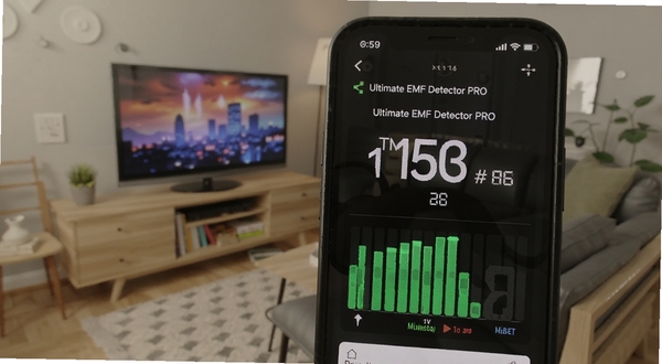 Ultimate EMF Detector PRO 实时读数界面特写,手机屏幕显示大号微特斯拉数值与动态条形指示,背景为居家客厅场景,主体手机位于画面中央偏右