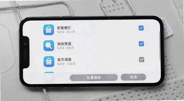 可萌精选安装包管理界面,手机屏幕显示安装包列表,每行左侧是应用图标,中间是应用名称和文件大小,右侧有勾选框,底部有批量删除按钮,背景为浅灰色工作台质感桌面,画面干净整洁,突出“清理”与“有序”的视觉感受