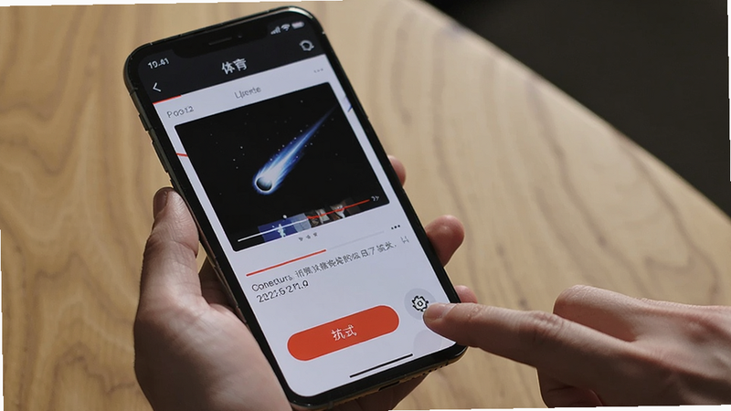 手机屏幕上显示彗星体育播放界面,但画面出现黑屏,下方有重试按钮,旁边一只手正在点击设置图标,背景为木桌,光线柔和