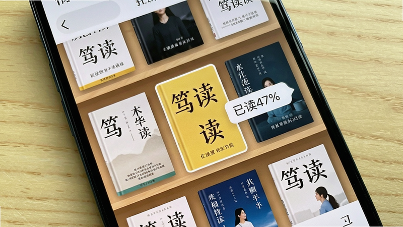 手机屏幕上显示笃读的书架界面,多本书籍封面整齐排列,中间有一本被高亮选中,旁边弹出“已读47%”的进度标签,背景为浅色木纹。