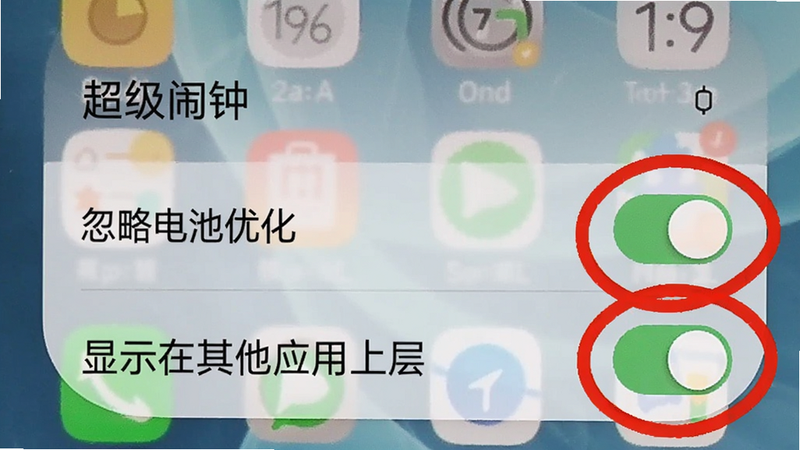 手机屏幕截图显示超级闹钟的权限设置页面,背景是一张模糊的手机桌面,重点突出“忽略电池优化”和“显示在其他应用上层”两个开关为绿色开启状态,周围用红色圆圈标注,画面简洁明了。