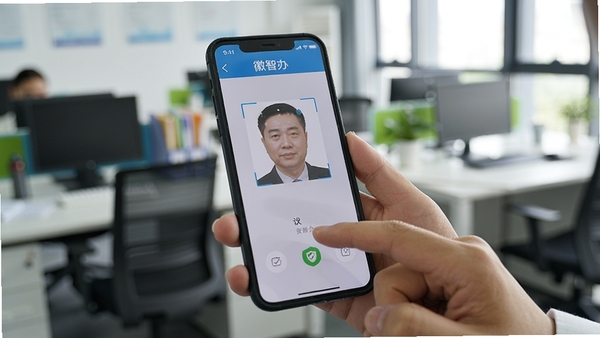 用户使用手机操作徽智办应用进行实名认证的场景,真人手部持手机,屏幕显示人脸识别框,背景为模糊的办公室环境,光线充足,突出手机屏幕内容,屏幕中需有