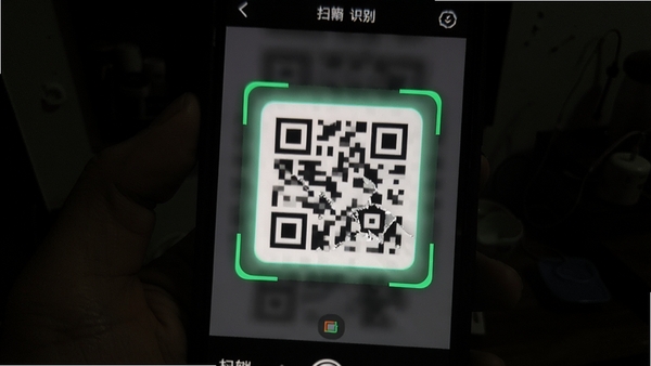 展示二维码扫扫识别软件在光线较暗环境下扫描模糊二维码的场景,手机屏幕上的扫描框对准一个有些破损的二维码,软件界面显示正在识别中,周围环境偏暗,但手机屏幕亮度较高,突出软件在弱光环境下的识别能力,画面真实自然。