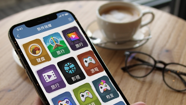 大转盘新决定软件功能展示图,手机屏幕特写显示应用内丰富的模板库界面,屏幕上排列着美食、旅行、影视、游戏等彩色图标方格,每个方格下方有白色文字标签,背景虚化的桌面上摆放着一杯咖啡和眼镜,画面风格写实,光线柔和,突出屏幕内容的清晰与丰富,产品界面截图风格