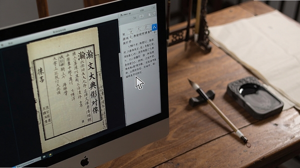 瀚文大典影像对照功能特写,电脑屏幕左侧显示古籍扫描原页,右侧显示对应文字文本,鼠标指针悬停在对照区域,背景为一张古木书桌,摆放着笔墨纸砚,突出学术研究氛围