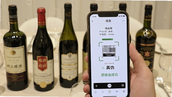 喝臻酒扫描酒瓶条形码的实拍演示图,手机屏幕显示识别成功结果,界面展示酒品名称、产地与真伪标识,背景为餐桌上的多款名酒,画面清晰明亮
