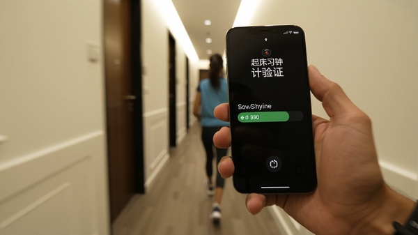 起床闹钟必醒计步验证界面,手机显示步数进度条,背景为室内走廊,用户手持手机行走,画面动态感强,展示真实使用场景