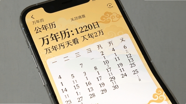 展示万年历天天看手机软件界面的全貌截图,画面主体为手机屏幕内清晰显示的日历主界面,上方显示公历与农历日期对照,背景区域为淡雅的暖黄色调和传统的祥云纹饰,整体风格简洁明亮,适配Boogu模型生成。