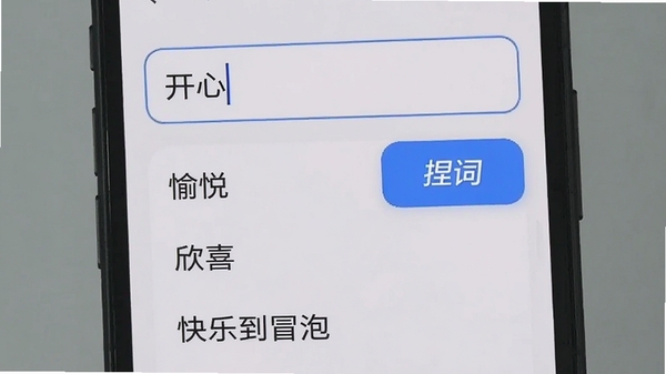 智能联想功能演示截图,手机屏幕显示输入框“开心”,下方列出多个联想词条,如“愉悦”“欣喜”“快乐到冒泡”,背景为浅灰色,界面带有蓝色高亮按钮,突出“捏词”品牌标识,画面清晰直观