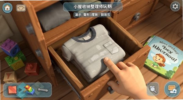 演示小屋收纳整理师物理模拟玩法,屏幕中一双手指正在拖动一件T恤,将其折叠后放入木柜抽屉,旁边有散落的积木和绘本,界面显示物品需按形状摆放,光影自然,画风3D卡通,细节丰富
