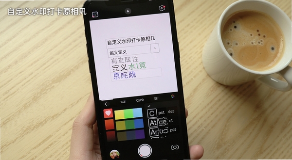 自定义水印打卡原相机的水印编辑界面截图,展示用户正在输入自定义文字并选择字体颜色的操作过程,屏幕下方有颜色调色盘和字体样式列表,背景为浅色木纹桌面,旁边放有一杯咖啡,画面突出编辑功能的直观与便捷,包含“自定义水印打卡原相机”文字标识