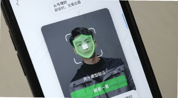 头号理财 移动端交易界面实拍图,画面展示正在进行的刷脸验证登录流程,背景为手机硬件特写,强调安全性与便捷性,浅色调背景搭配绿色安全盾牌图标,写实摄影风格