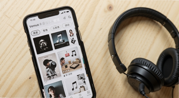 Vemus未音音乐库管理界面,手机屏幕展示专辑网格与歌曲列表,分类标签清晰,背景为浅色木质桌面与耳机,体现本地音乐整理场景
