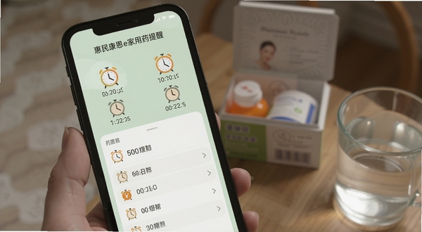 惠民康恩e家用药提醒设置页面截图风格,手机界面显示多个时间闹钟图标与药品名称列表,背景为淡绿色,旁边有药盒与温水杯,画面生活化