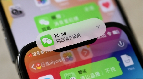 灵动岛消息通知提醒界面,手机顶部胶囊弹出微信消息图标与文字预览,背景为聊天界面虚化效果,画面聚焦于手机顶部区域,色彩鲜明
