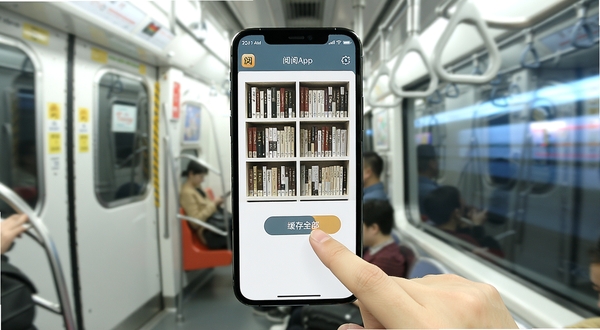 已阅App在手机屏幕上显示书架界面,旁边有一只手正在点击“缓存全部”按钮,背景是地铁车厢与窗外的流动光影,画面风格写实明亮,突出移动阅读场景,软件名称已阅出现在手机顶部状态栏