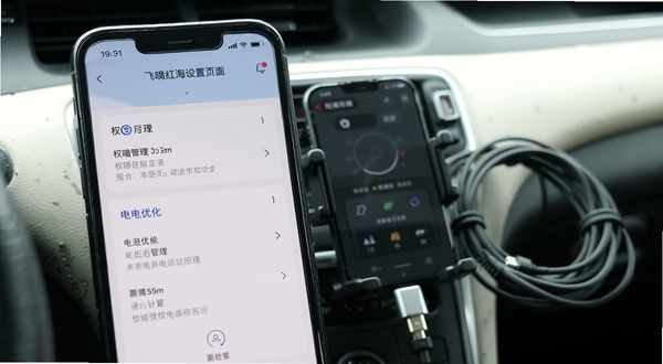 飞嘀红海设置页面操作示意,手机屏幕展示权限管理与电池优化选项,背景为车内手机支架与充电线,画面清晰直观,体现移动端使用场景
