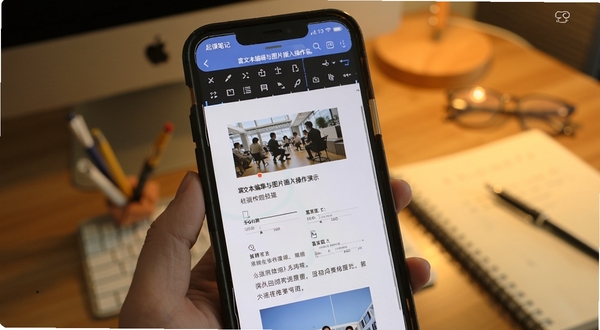 起课笔记 富文本编辑与图片插入操作演示 画面主体为手机屏幕显示编辑工具栏与图文混排效果 背景区域为暖色调桌面 适配Boogu模型生成