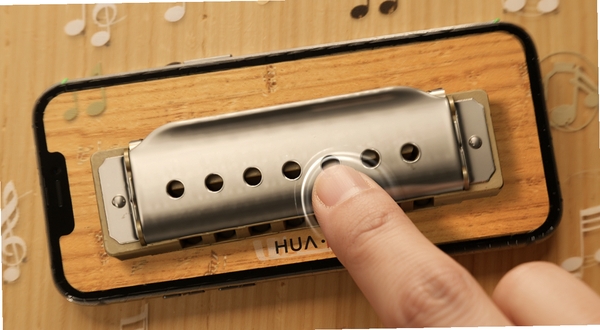 HUA pocket harmonica手机口琴界面展示,屏幕中央排列十个音孔,暖色木质背景,柔和灯光,手指轻触音孔的动态效果,清新简约风格