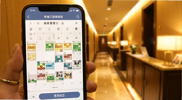 哗省订房商家版房态管理界面特写,画面主体为手机屏幕内的彩色房态日历,背景区域为虚化的酒店走廊,色调温暖明亮,突出实时更新与便捷操作场景