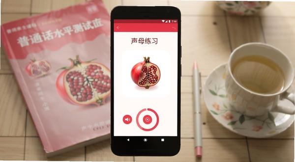 一部安卓手机屏幕中央显示石榴普通话APP的课程界面,界面设计简洁清新,以石榴红和白色为主色调,屏幕上方有“声母练习”字样,下方有录音按钮和评分环,背景是模糊的书桌场景,桌上放着一本普通话水平测试教材和一杯茶,画面光线柔和,适合作为软件下载站的预览图