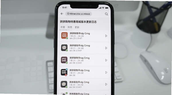 拼拼购物特惠商城版本更新日志页面截图,画面中手机屏幕展示更新记录列表,背景为浅灰色办公桌面,风格简洁