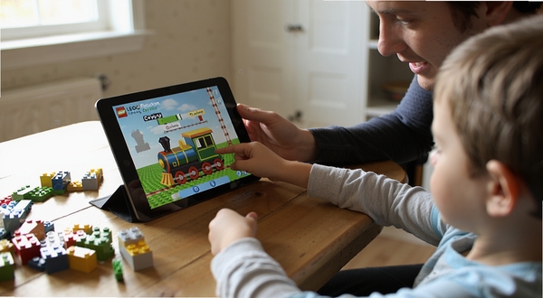 LEGO Education Coding Express 家长与孩子一起使用平板进行积木编程互动的场景,温馨家庭氛围,屏幕显示彩色小火车界面,乐高积木散落在桌面上,自然光线,真实摄影风格