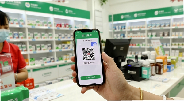 一位四川参保群众在药店柜台前使用四川医保APP展示医保电子凭证二维码进行扫码购药,画面明亮温馨,手机屏幕清晰可见二维码界面,背景是整洁的药店货架