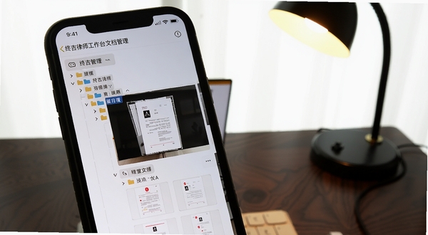 终吉律师工作台文档管理界面,手机屏幕显示文件夹树状结构与PDF预览缩略图,背景为深色木质桌面,有台灯照明,画面突出文档管理的条理性
