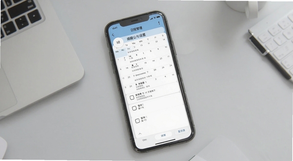攀登精英移动端操作界面,展示提醒设置与日程管理页面,手机屏幕中显示日历视图与待办事项列表,背景为浅灰色办公桌面风格,画面清晰整洁