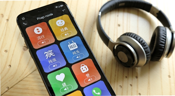 手机来电铃声多免费软件内铃声分类浏览界面,画面展示一部手机屏幕中排列着流行、经典、搞笑、纯音乐等分类卡片,卡片带有彩色图标和试听按钮,背景为浅色木质桌面,旁边放着一副耳机,整体氛围轻松明快