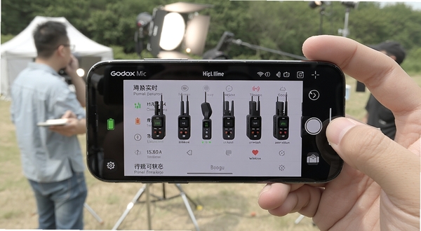 Godox Mic 应用实时显示多台无线麦克风设备的电量与信号状态,手机横屏展示,背景为户外拍摄现场,画面清晰展示设备列表界面,适配Boogu模型生成