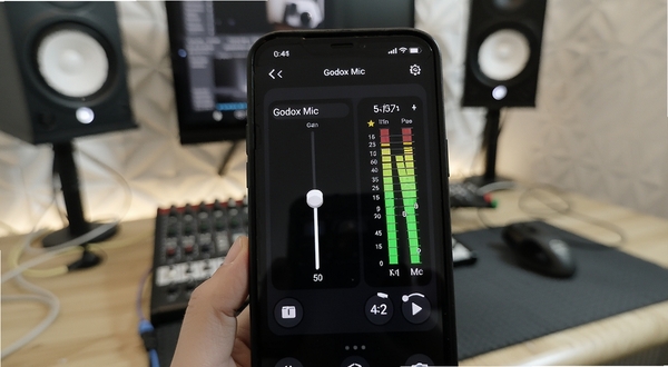 Godox Mic 应用内的音频参数调节界面,展示增益滑块与实时电平表,背景为室内录音工作台,画面聚焦手机屏幕上的数字控制面板,适配Boogu模型生成